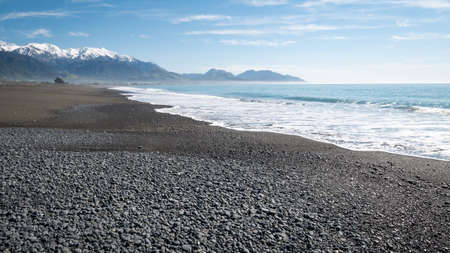 Remote beach with azure waters, blue skies and mountains in backdrop. Shot with waves coming in made in Kaikoura peninsula, New Zealandの写真素材