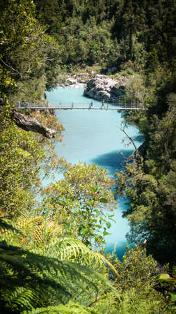 River gorge with turquoise waters and swing bridge leading above it. Portrait shot made at Hokitika gorge, West Coast, New Zealandの写真素材