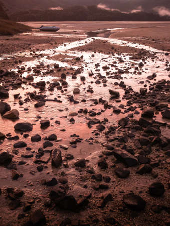 Crimson sunset in tropical inlet bay with deserted boat in frame. Portrait shot made in Abel Tasman National Park, New Zealandの写真素材