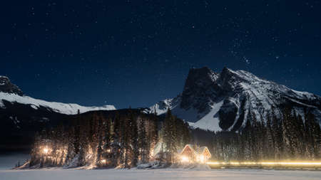Iluminated alpine huts amongst the trees under the mountains and sky full of stars, winter, Canada