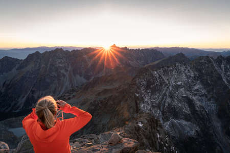 Woman photographing sunset in alpine environment surrounded by rocky mountains and peaks, Europeの写真素材