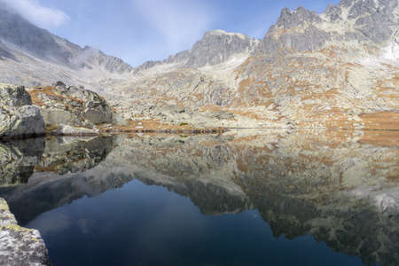 Still alpine lake reflecting rocky mountains with autumn colors surrounding it, Slovakia, Europeの写真素材