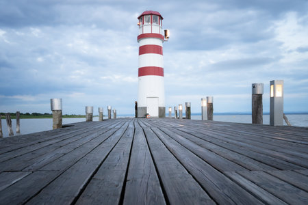 Red and white lighthouse on a cloudy morning with wooden jetty leading to it , Austriaの写真素材