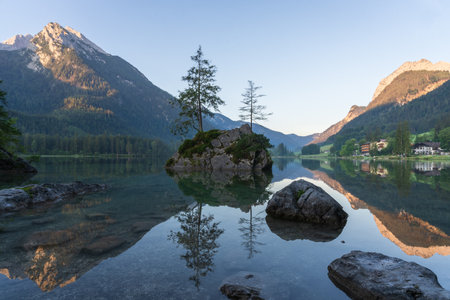 Crystal clear alpine tarn with rocky islands with tree on them during sunrise, Hintersee, Germanyの写真素材