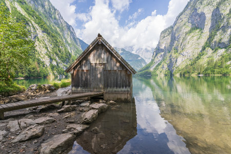Old wooden boathouse on a still pristine alpine lake surrounded by mountains, Obersee, Germanyの写真素材