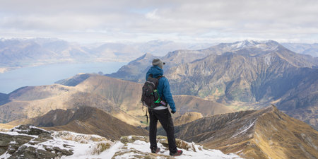 Male hiker standing on top of the mountain enjoying views on beautiful alpine landscape with lake.