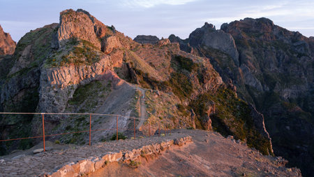 Hiking trail with mountains in backdrop catching soft orange light during sunrise, Madeira, Portugalの写真素材