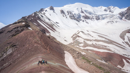 Group of hikers taking break in mountain saddle under snowy ridgeline, Pamir Mountains, Kyrgyzstan