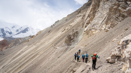 Tourists hiking scree on the side of the mountain with snowy background, Pamir mountains, Kyrgyzstan