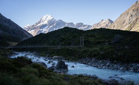 Beautiful alpine valley with glacial river, swing bridge and snowy mountain, Mt Cook, New Zealandの写真素材