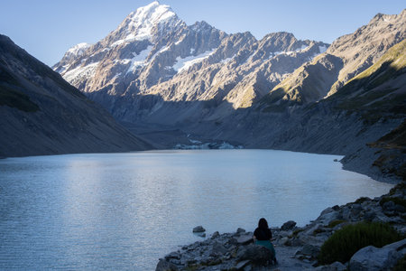 Woman sitting on a bank of glacial lake looking at a glaciers and mountain, Mt Cook, New Zealand