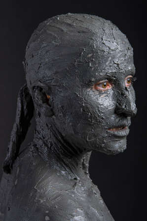 Statuesque woman in wet clay. Woman covered in wet clay. Spa treatment or scary Halloween mask?の写真素材