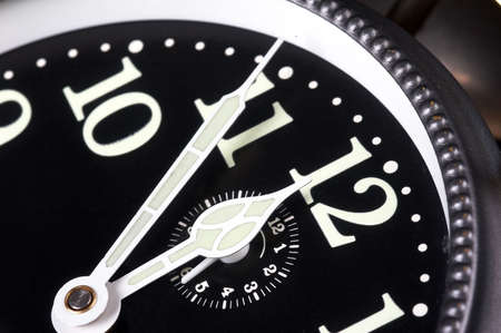 Old alarm clock showing five minutes to midnight on black background with black clock face and white needles - landscape formatの写真素材