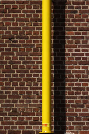 yellow pipe in front of a red brick wall, the yellow pipe is wet paint
