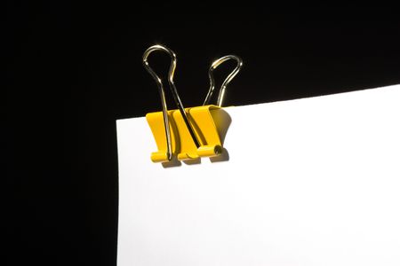 Yellow paper-clip on a white sheet, black backgroundの写真素材