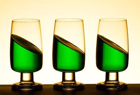 Three glasses containing green cocktail looking impossible as they are all at an angle to the horizontalの写真素材