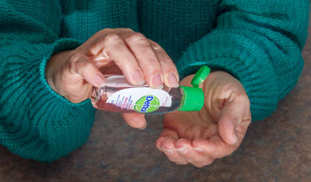 Woman applies hand sanitizer durin g the pandemic in a poace where she is unable to wash hands with soap and waterのeditorial素材