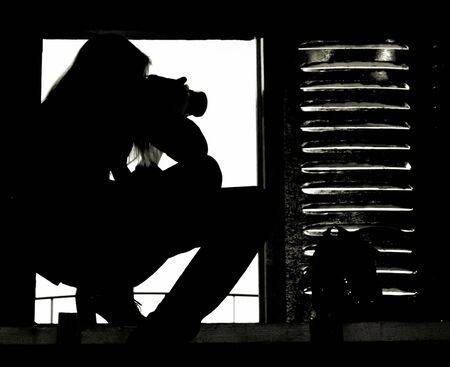 A silhouette of the professional girl-grapher taking pictures from the attic windowの写真素材