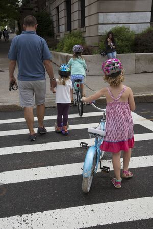 Young children on bicycles crossing the street. A rear viewのeditorial素材
