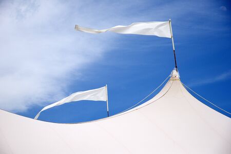Marquee roof with flags blowing in the wind against a blue skyの写真素材