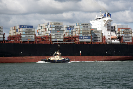 Container carrier ship with tugboat support on Southampton Water England UK