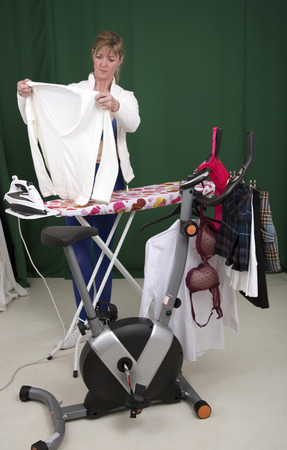 Woman ironing clothes using exercise bike as a clothes horseの写真素材