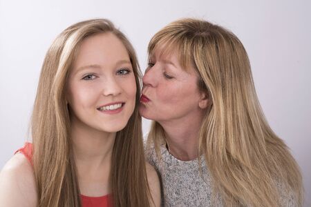 Portrait of a mother kissing her teenage daughterの写真素材