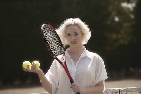 PORTRAIT OF A YOUNG TENNIS PLAYER - A young female tennis player with fair hair holding a raquet and...
