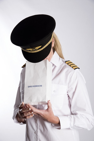 Woman using a sickness bag - September 2016 - A uniformed female pilot feeling nauseous using a paper sickness bagの写真素材