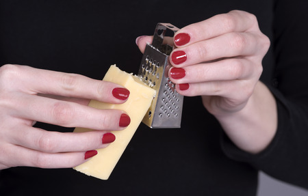 Woman with red nails holding a chunk of cheese and a small graterの写真素材