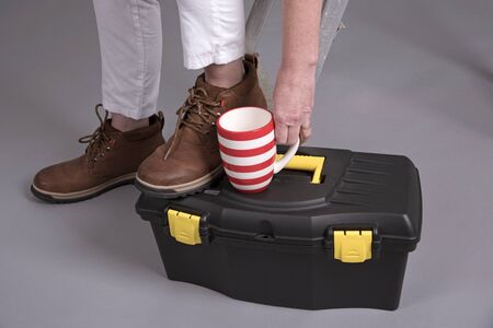 Worker's boots with a tea mug and toolboxの写真素材