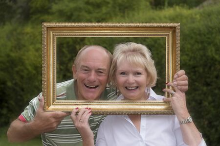 Portrait of an elderly couple playing with a picture frame in a garden settingの写真素材