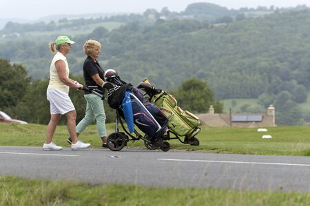 Lady golfers in the South Cotswolds region of England UK Crossing a country road with their electric golf caddies. Auugust 2017のeditorial素材