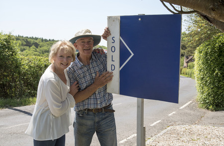 Couple standing with a sold sign outside their home