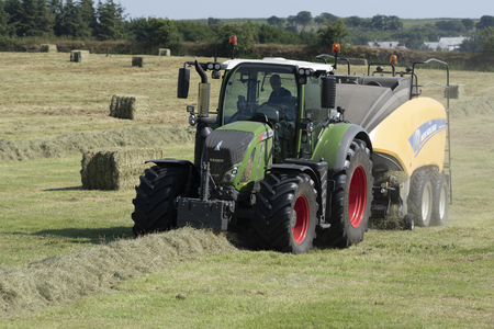 Baling machine working at harvest time baling straw on a farm at Dartmoor, Devon, England, UKのeditorial素材
