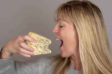 Blonde woman eating and enjoying a wedge of blue cheese