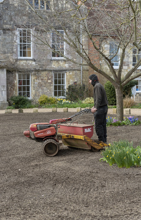 Winchester, Hampshire, England UK. March 2019. Landscape gardener riding on a seed spreader and roller to form a new lawn.のeditorial素材