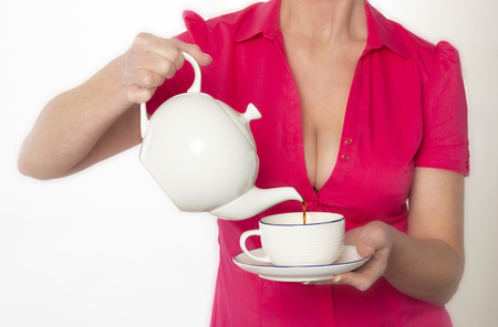 Southern England UK.  Attractive woman wearing a revealing red shirt pouring a cup of teaの写真素材