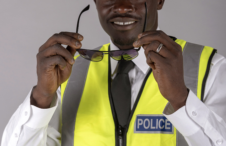 Portrait of a smiling police officer in uniform and holding a pair of dark glasses.