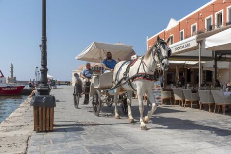 Chania, Crete, Greece, June 2019. An open top horse drawn carriage with driver and passenger in old town Chania, Crete.のeditorial素材