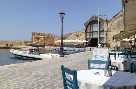 Chania, Crete, Greece. June 2019. The Old Venetian Harbour with a restaurant empty table and chairs on the waterfront.のeditorial素材