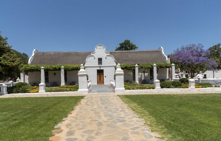 Faure, Stellenbosch, Western Cape, South Africa. Dec 2019. The homestead of the Vergenoegd Low wine estate. Cape Dutch style building with a Jacaranda tree in bloom.のeditorial素材