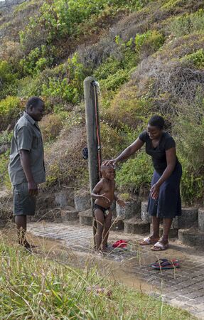 Western Cape, South Africa. Dec 2019. Little boy taking a shower helped by his mother aand father after taking a dip in the Indian Ocean while on holidayのeditorial素材