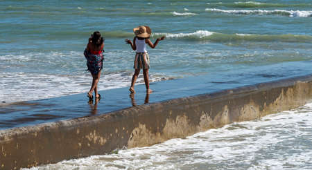 Strand, Somerset West, Western cape, South Africa. Dec 2019. Young girls having fun walking along the sea wall at Strand, Somerset West, South Africaのeditorial素材