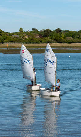 Lymington, Hampshire, England, UK. May 2020. Young boy and girl learning to handle their Optomist sailboats on Lymington River in the New Forest, Hampshire, UK.のeditorial素材