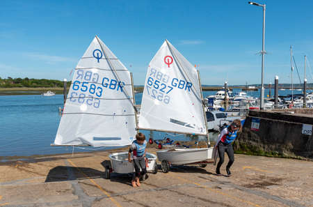 Lymington, Hampshire, England, UK. May 2020. Young boy and girl learning to handle their Optomist sailboats on Lymington River in the New Forest, Hampshire, UK. Using trailers to bring boats ashore.のeditorial素材