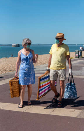 Southsea, Portsmouth, England, UK. May 2020. Elderly couple wearing medical masks carrying picnic equipment on the promenade at Southsea, UK.のeditorial素材