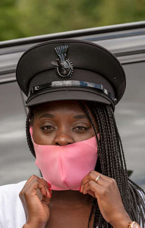 England, UK. 2020.   Portrait of a woman chauffeur with uniform cap and braided hair adjusting her...
