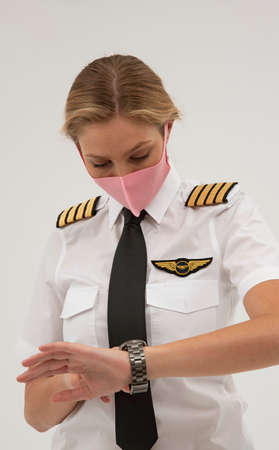 Wiltshire, England, UK. August 2020.  Airline pilot checking her wristwatch and wearing a face mask...