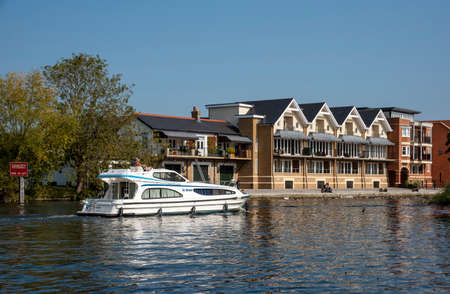 Eton, Buckinghamshire, England, UK. 2020. Cabin cruiser passing modern housing along the River Thames seen from Windsor looking to the Eton riverside.のeditorial素材